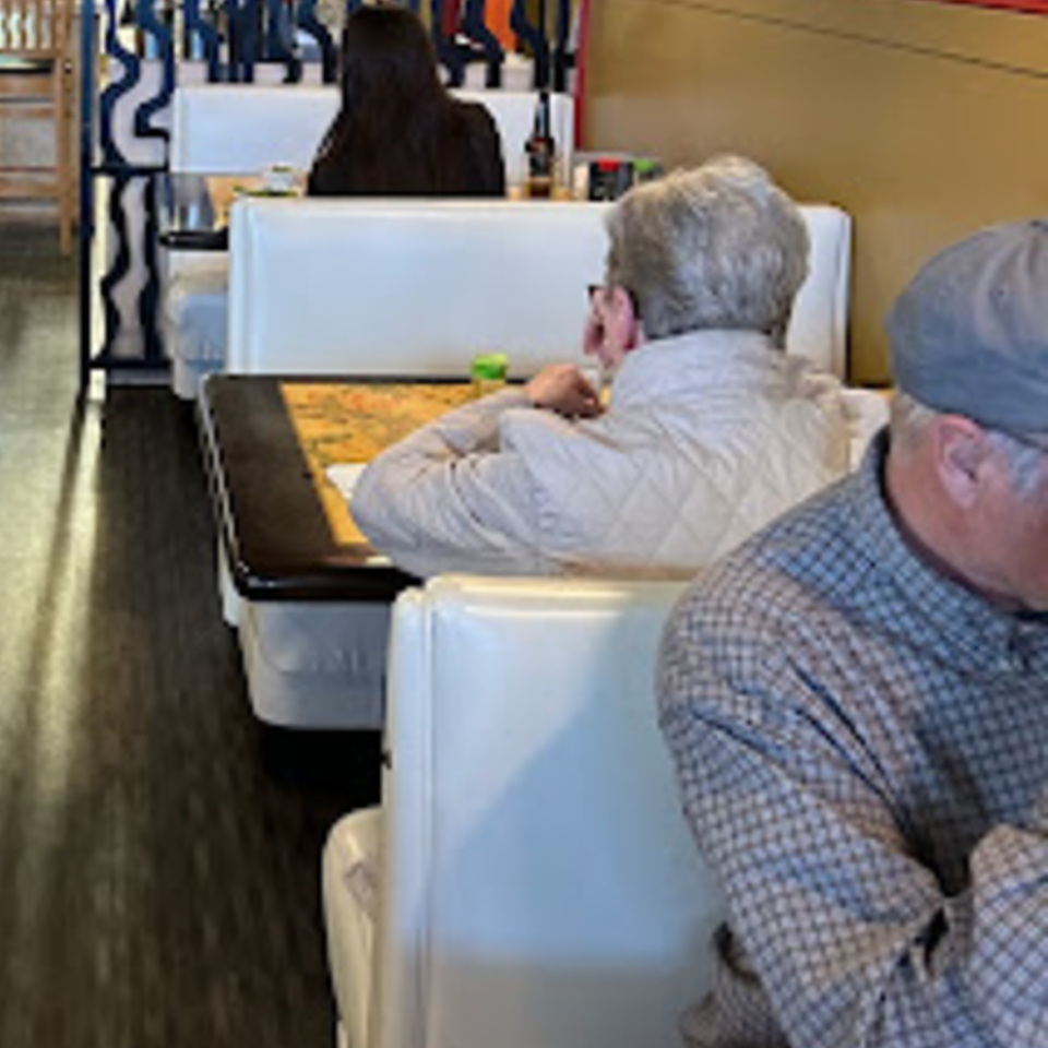 Diners seated in white booths at Tokyo Garden, with a man in a plaid shirt in the foreground.
