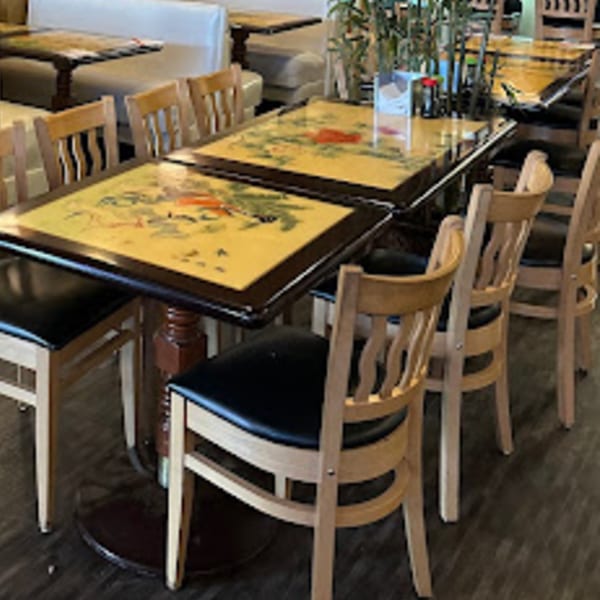 Dining area at Tokyo Garden with tables featuring decorative tops and light wood chairs with dark seats.